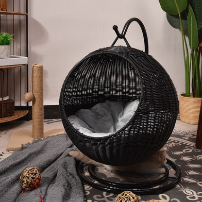 Black woven cat hammock with a soft cushion inside, placed on a patterned rug.