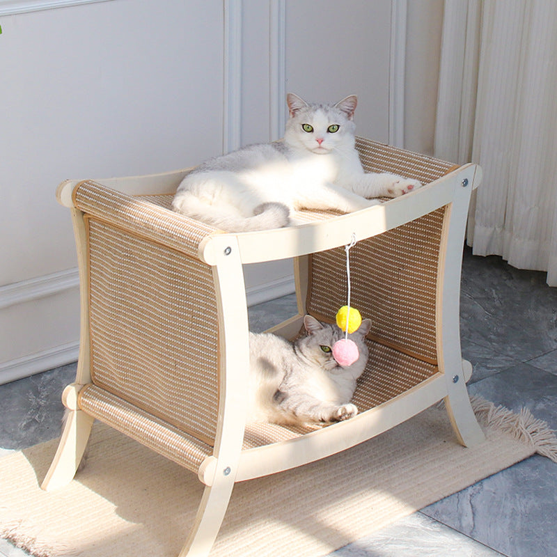 Two cats on a wicker pet bed with toys hanging from it, in a room with light-colored walls and a rug.