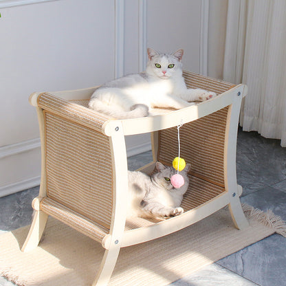 Two cats on a wicker pet bed with toys hanging from it, in a room with light-colored walls and a rug.