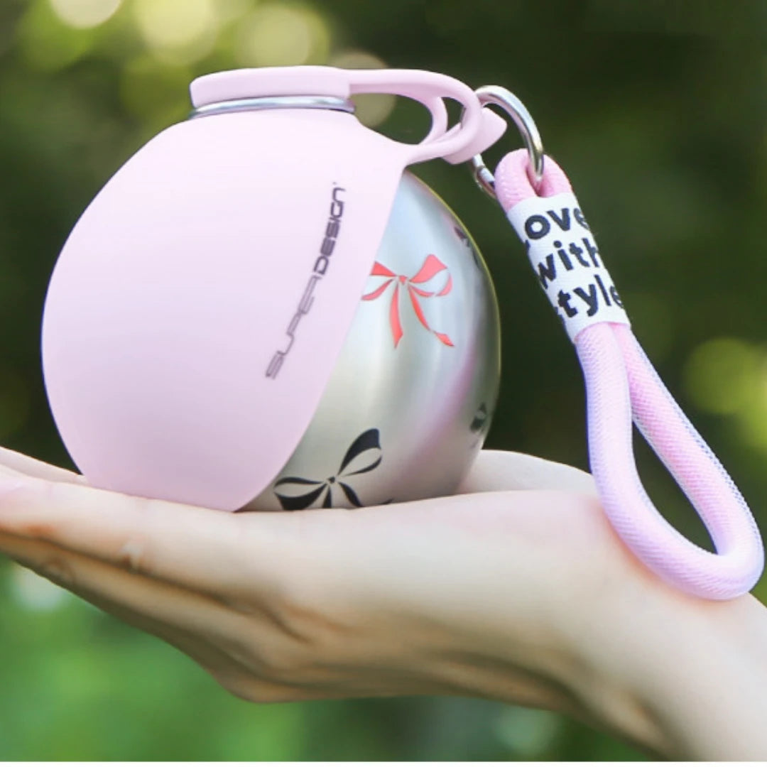 Pink spherical keychain with a lanyard on a blurred green background