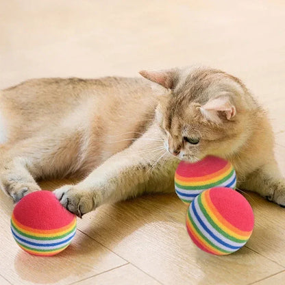 Cat playing with rainbow-striped balls on a wooden floor