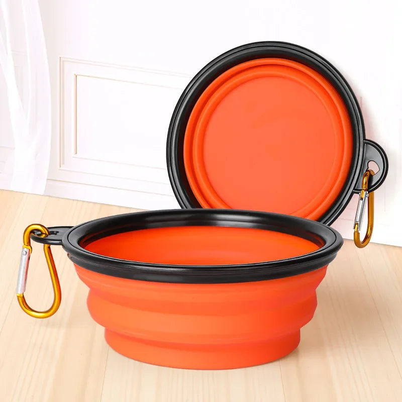 Orange and black collapsible pet bowl with carabiner on a light wooden surface.
