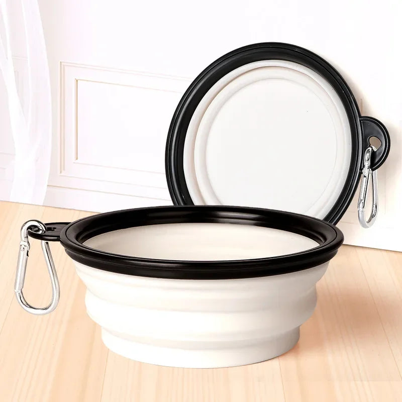 Collapsible black and white dog bowl with carabiner on a wooden surface