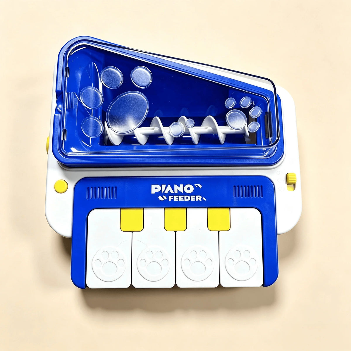 A blue and white pet toy feeder shaped like a piano keyboard, with paw print buttons and a transparent lid showing plastic treats inside, photographed on a plain beige background.