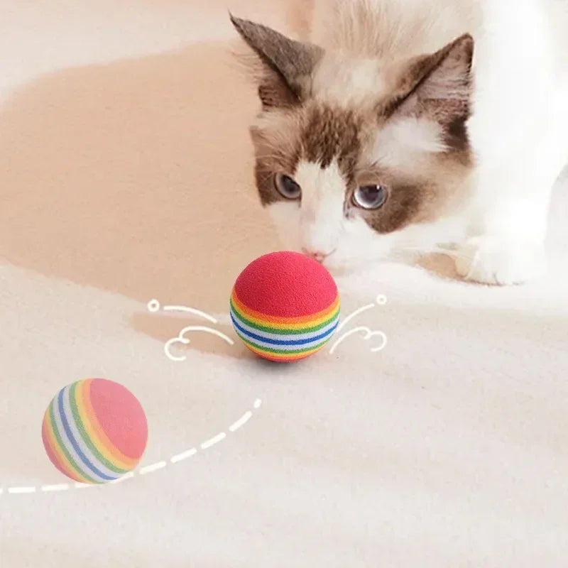 Cat playing with a colorful striped ball on a soft surface