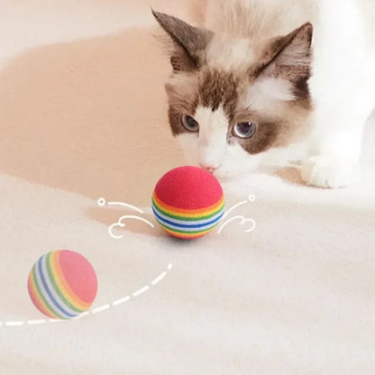 Cat playing with a colorful striped ball on a soft surface