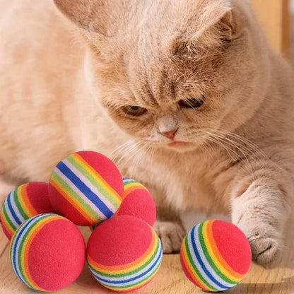 Cat playing with rainbow-striped balls on a wooden surface