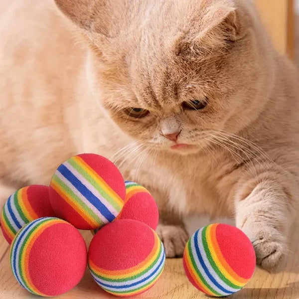 Cat playing with rainbow-striped balls on a wooden surface