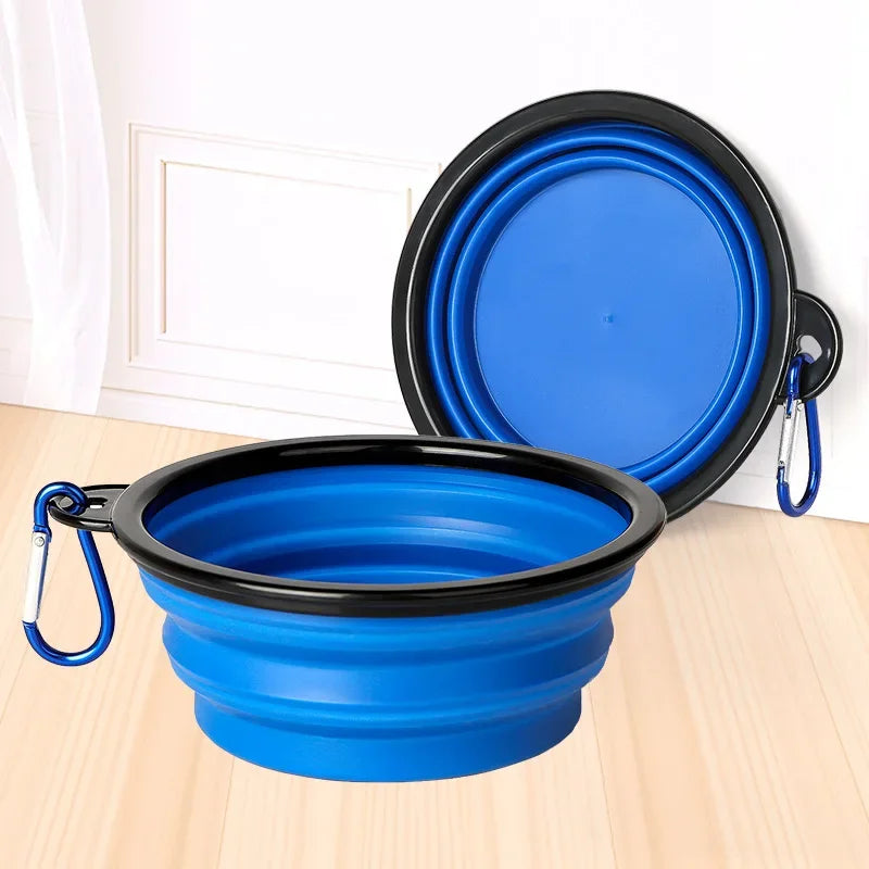 Blue and black collapsible pet bowl with carabiner on a light wooden surface.