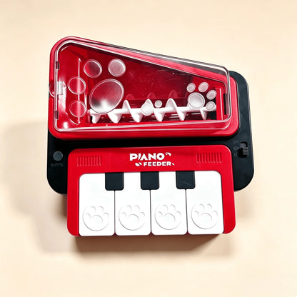 A red and black pet toy feeder shaped like a piano keyboard, with a transparent lid showing white plastic inner pieces and four white paw-print keycaps on a beige background.