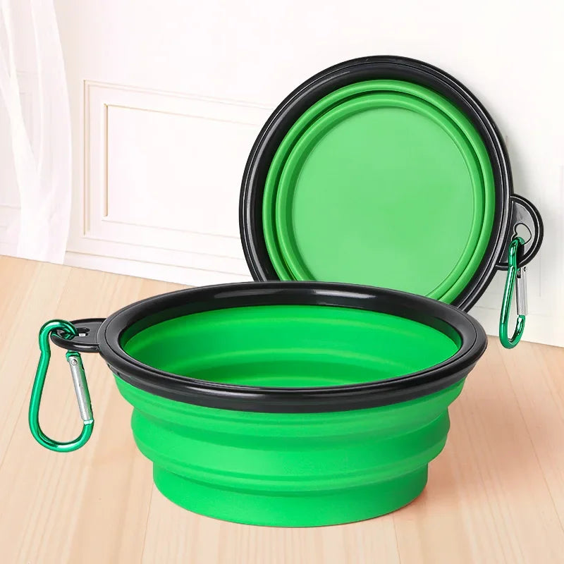Green and black collapsible travel bowl with carabiner on a wooden surface.