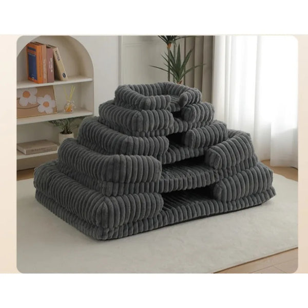 Stack of gray pet beds on a light-colored rug in a room with a bookshelf and plant.