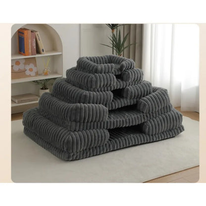 Stack of gray pet beds on a light-colored rug in a room with a bookshelf and plant.